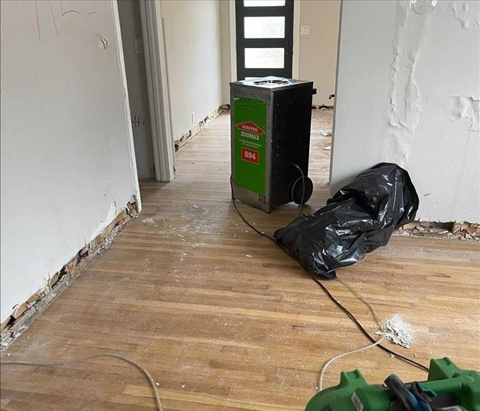 inside of home with baseboards ripped out, damage to walls, debris on floors, and servpro equipment 