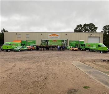 large group of employees in khaki pants & black shirts with SERVPRO vehicles staged in the back all in front of tan building